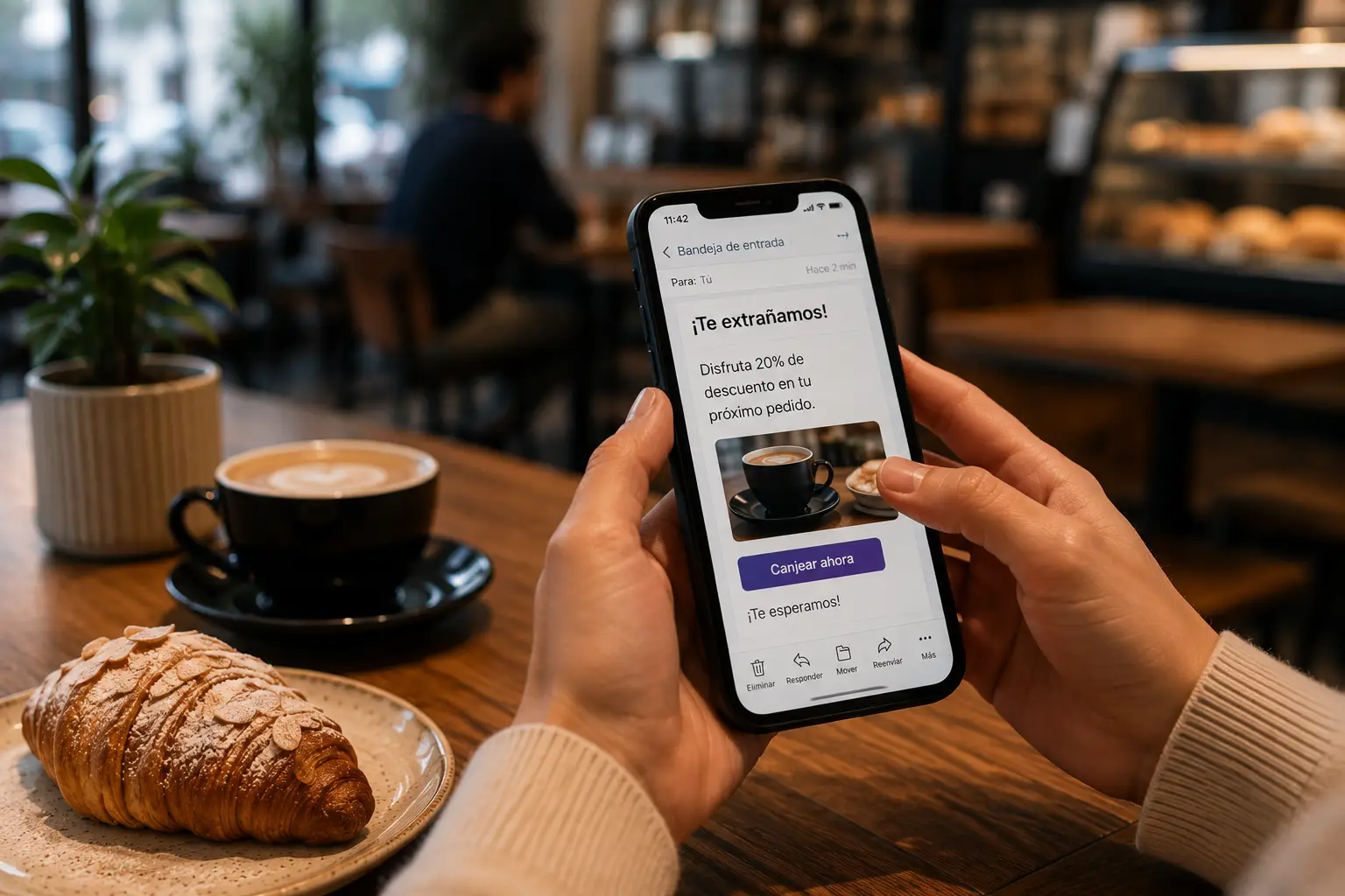 Cliente recibe un correo automatizado de fidelización en su teléfono móvil mientras disfruta de un café en una cafetería, ilustrando una campaña de marketing automatizado basada en el comportamiento del consumidor.